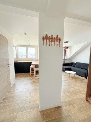 Un interno moderno con pavimento in legno, un divano nero, un tavolo bianco e un elemento decorativo a parete.
