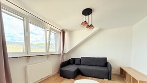 Ett modernt vardagsrum med en hörnsoffa, ett runt soffbord och ett stort fönster med gardiner.