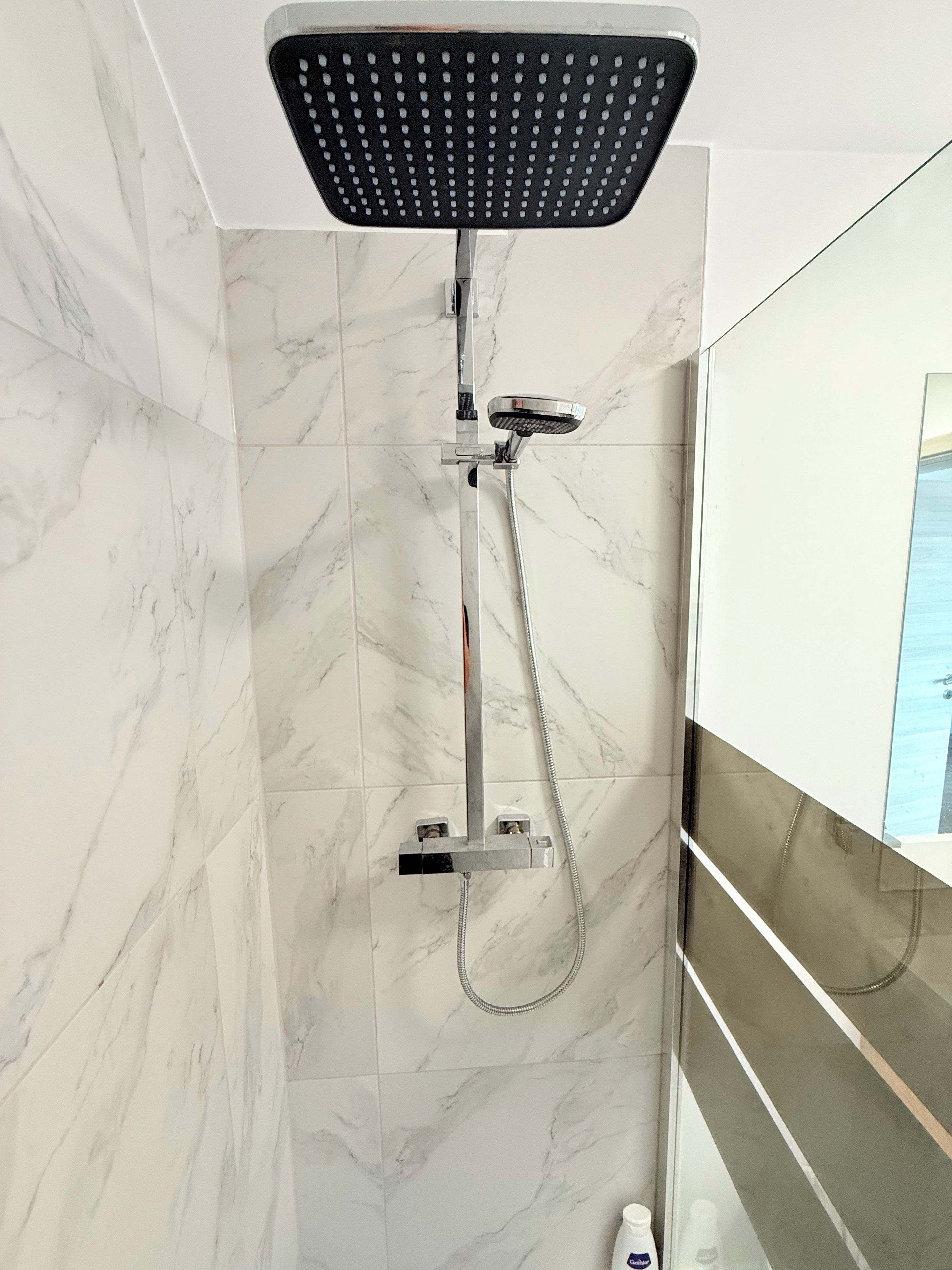 A modern bathroom with a shower, marble tiles, and a glass partition.