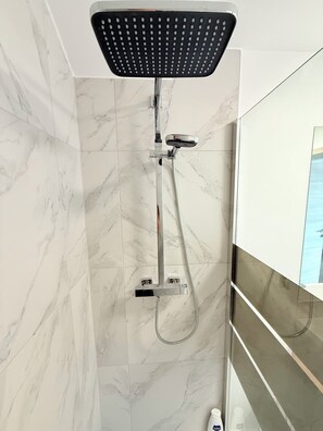 A modern bathroom with a shower, marble tiles, and a glass partition.