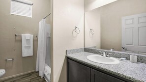 Ein Badezimmer mit Waschbecken, Spiegel, Handtuchhalter, Duschvorhang und Toilette.