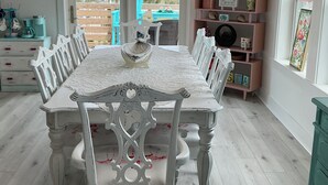 Uma sala de jantar com uma mesa e cadeiras brancas, um candelabro e vista para o exterior.
