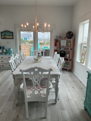 A dining area with a white table and chairs, a chandelier, and a view of the outside. - Beautiful Beach Home on the West End of Galveston with Beach across the street (Galveston)