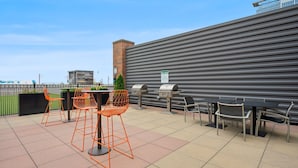 Area patio esterna con tavoli e sedie, un barbecue e vista sulla città.