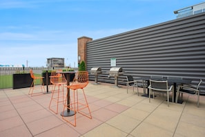 Eine Außenpatio-Terrasse mit Tischen, Stühlen, einem Grill und Blick auf die Stadt.