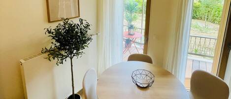 Un comedor con una mesa redonda, cuatro sillas, una planta en maceta, un cuadro enmarcado y vistas al exterior a través de una ventana.