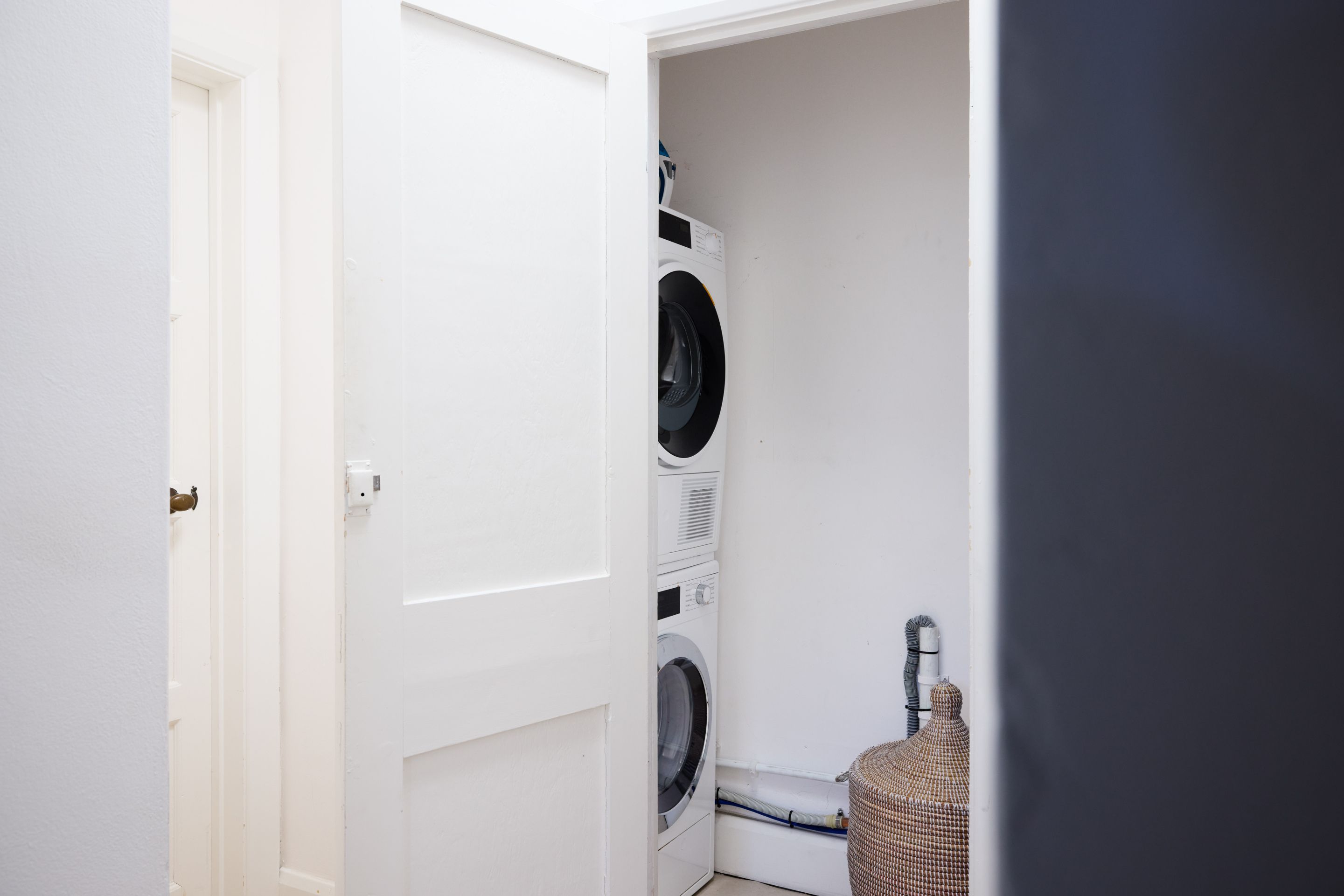A laundry room with a stacked washer and dryer, a wicker basket, and a white door.