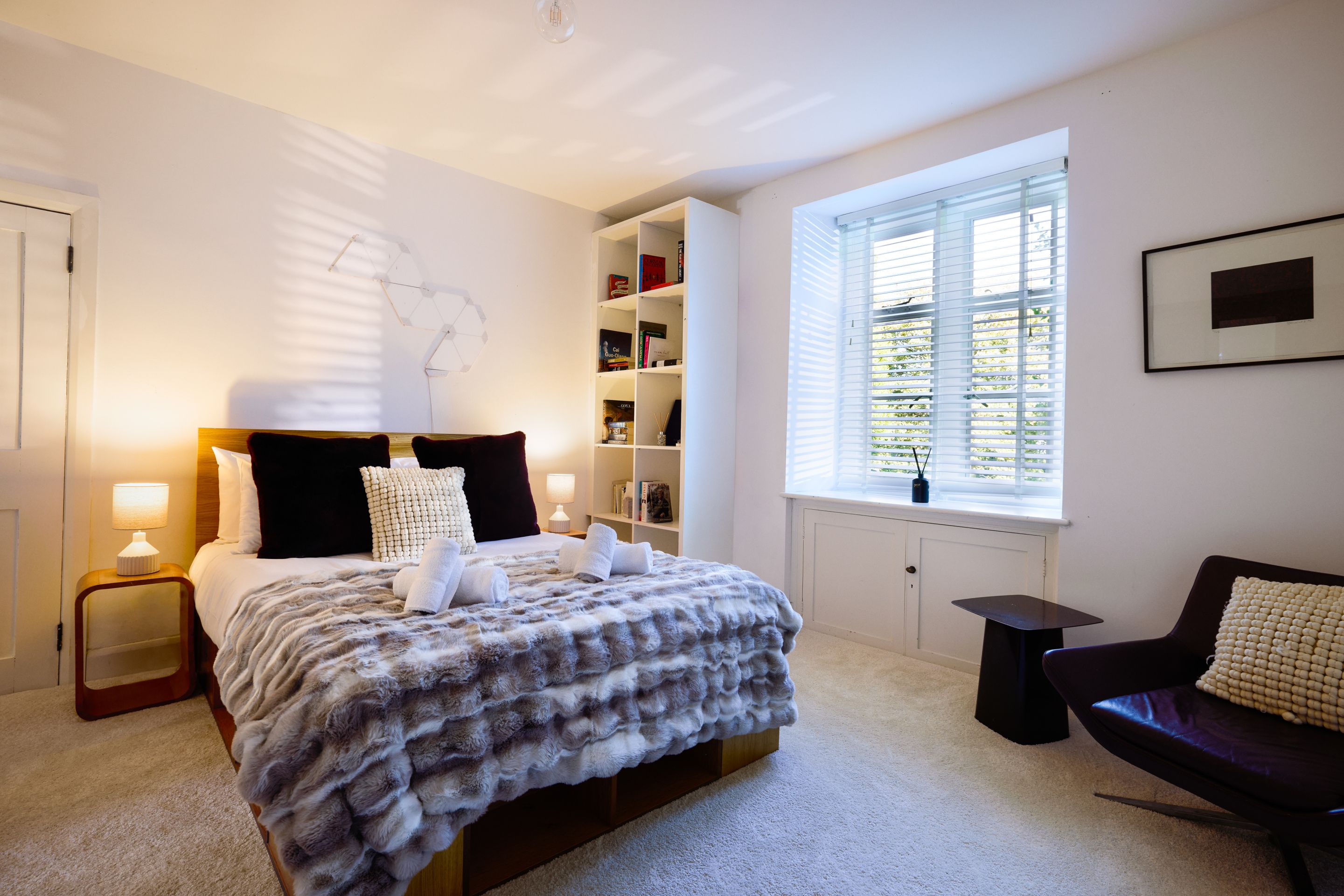 A bedroom with a bed, bedside tables, a bookshelf, a window, and a chair.