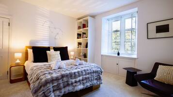 A bedroom with a bed, bedside tables, a bookshelf, a window, and a chair.