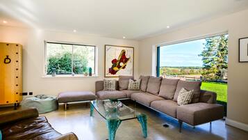 A modern living room with a sectional sofa, a glass coffee table, and a view of a park through large windows.