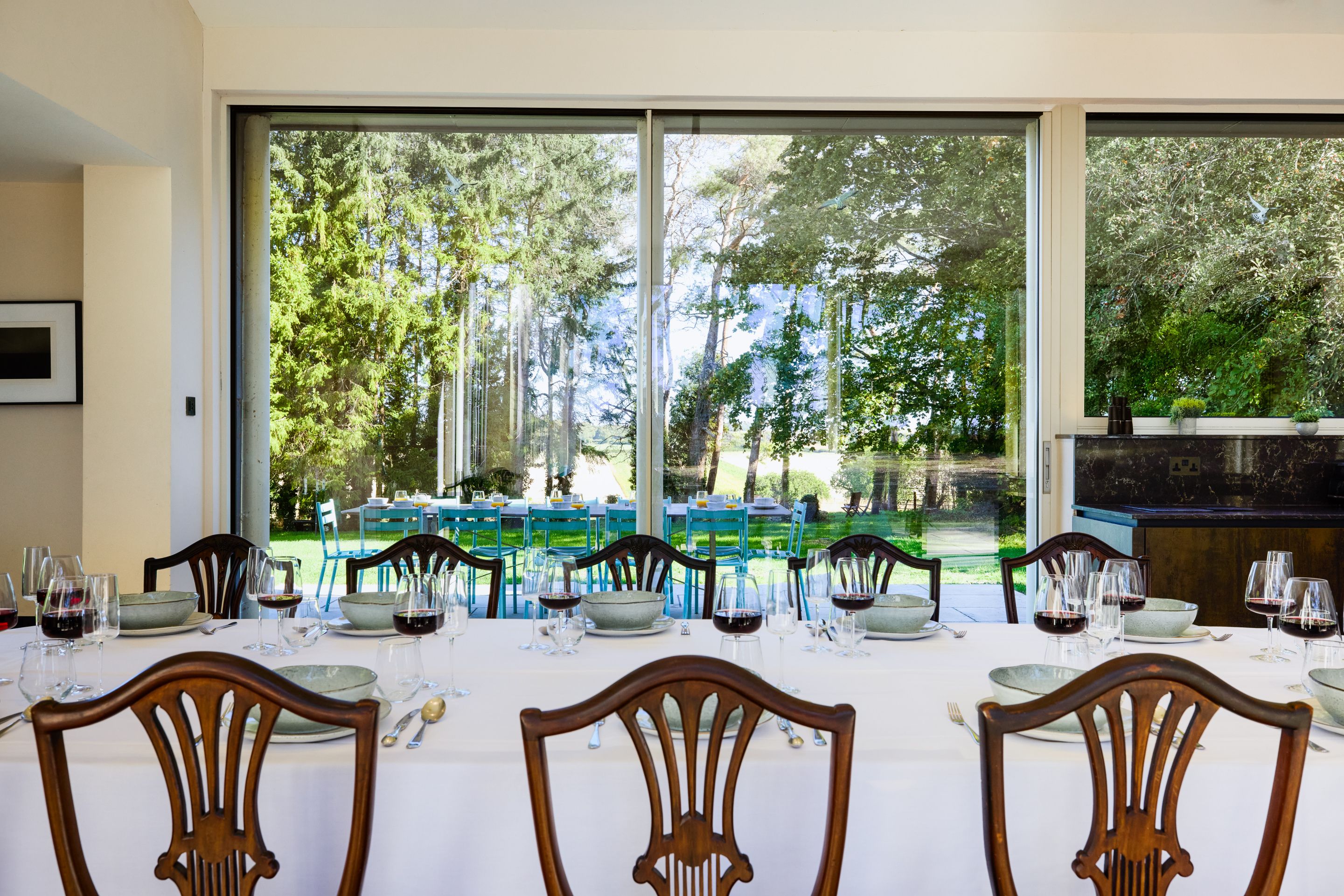 Un coin repas avec une table dressée pour six personnes, donnant sur un jardin arboré et équipé d’un barbecue.
