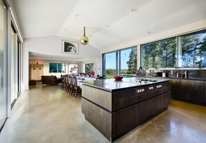 Una cocina moderna con una isla grande, comedor y ventanas amplias que ofrecen vistas al exterior.