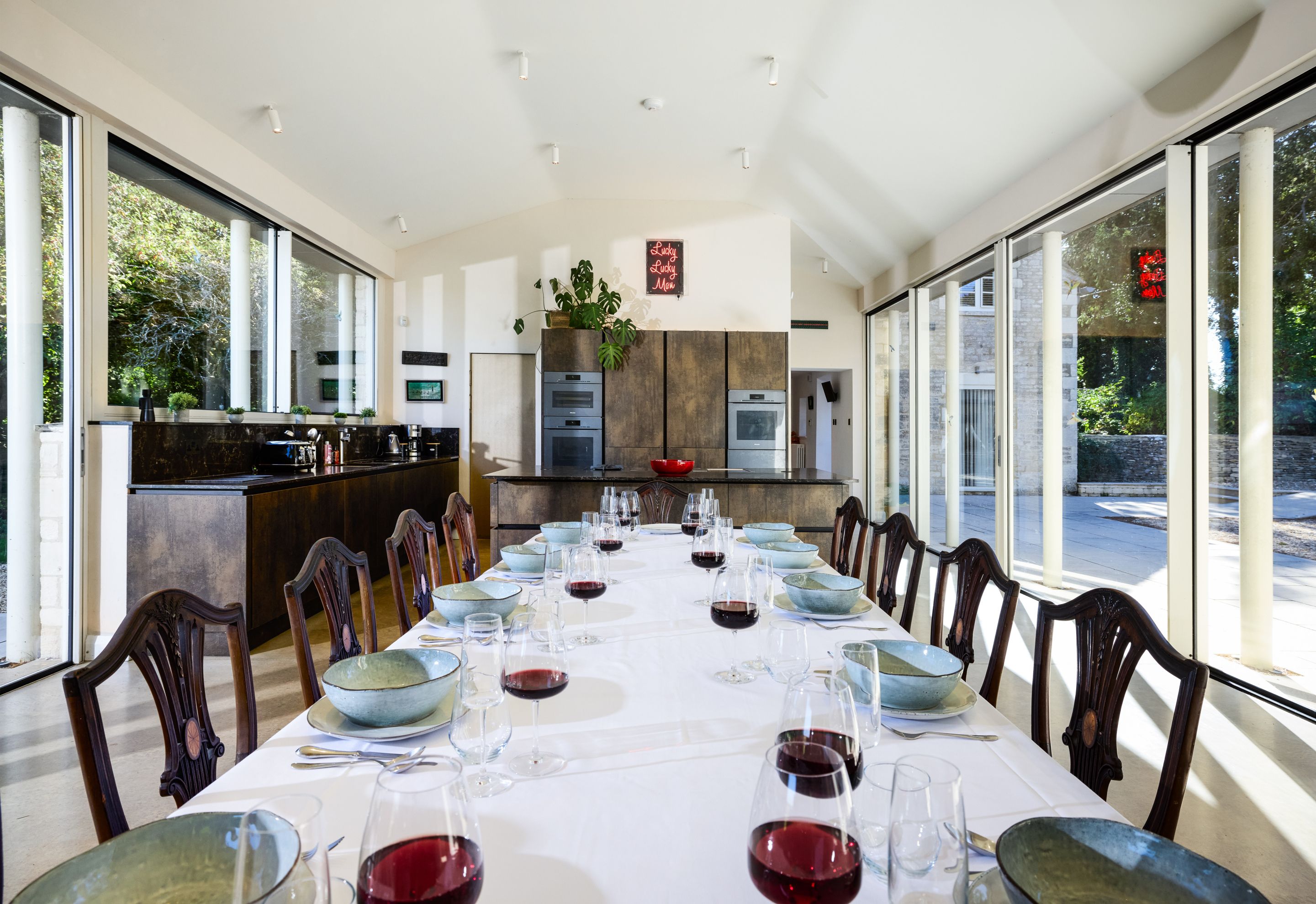 A modern dining room with a long table set for a meal, large windows, and a view of the outdoors.