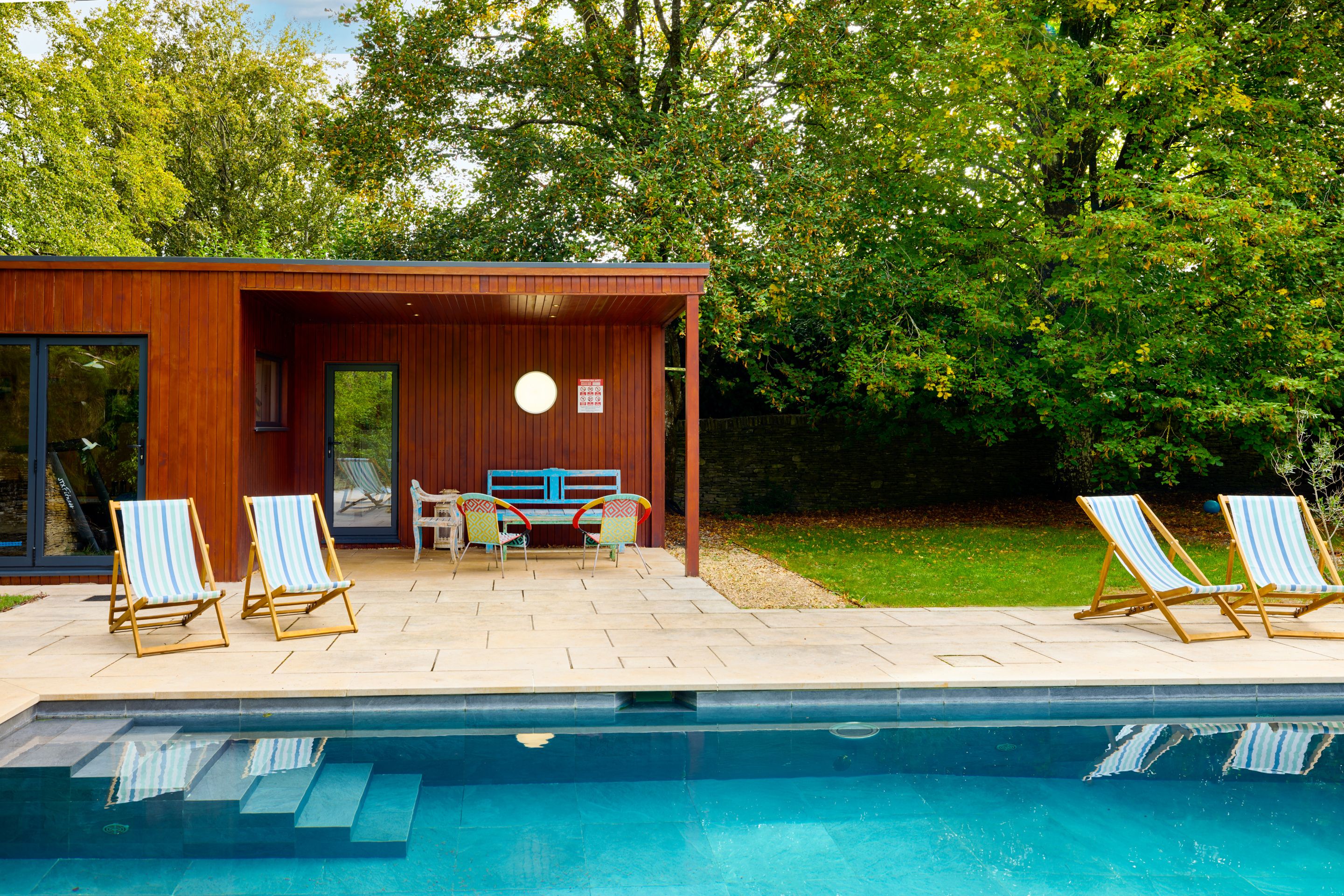 A modern outdoor pool area with a wooden deck, lounge chairs, and a small seating area.