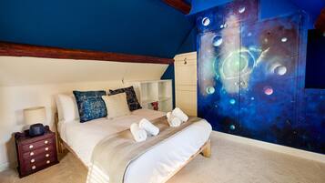 Een slaapkamer met een bed, nachtkastje, kapstok en een muur met een ruimtethema-muurschildering.