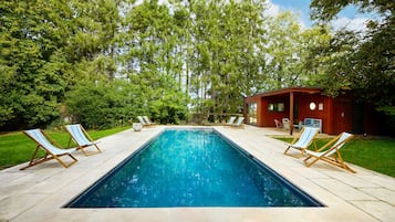 Una piscina rettangolare con acqua cristallina e trasparente, circondata da un solarium piastrellato. Due sdraio di legno con cuscini a righe si trovano su entrambi i lati della piscina.