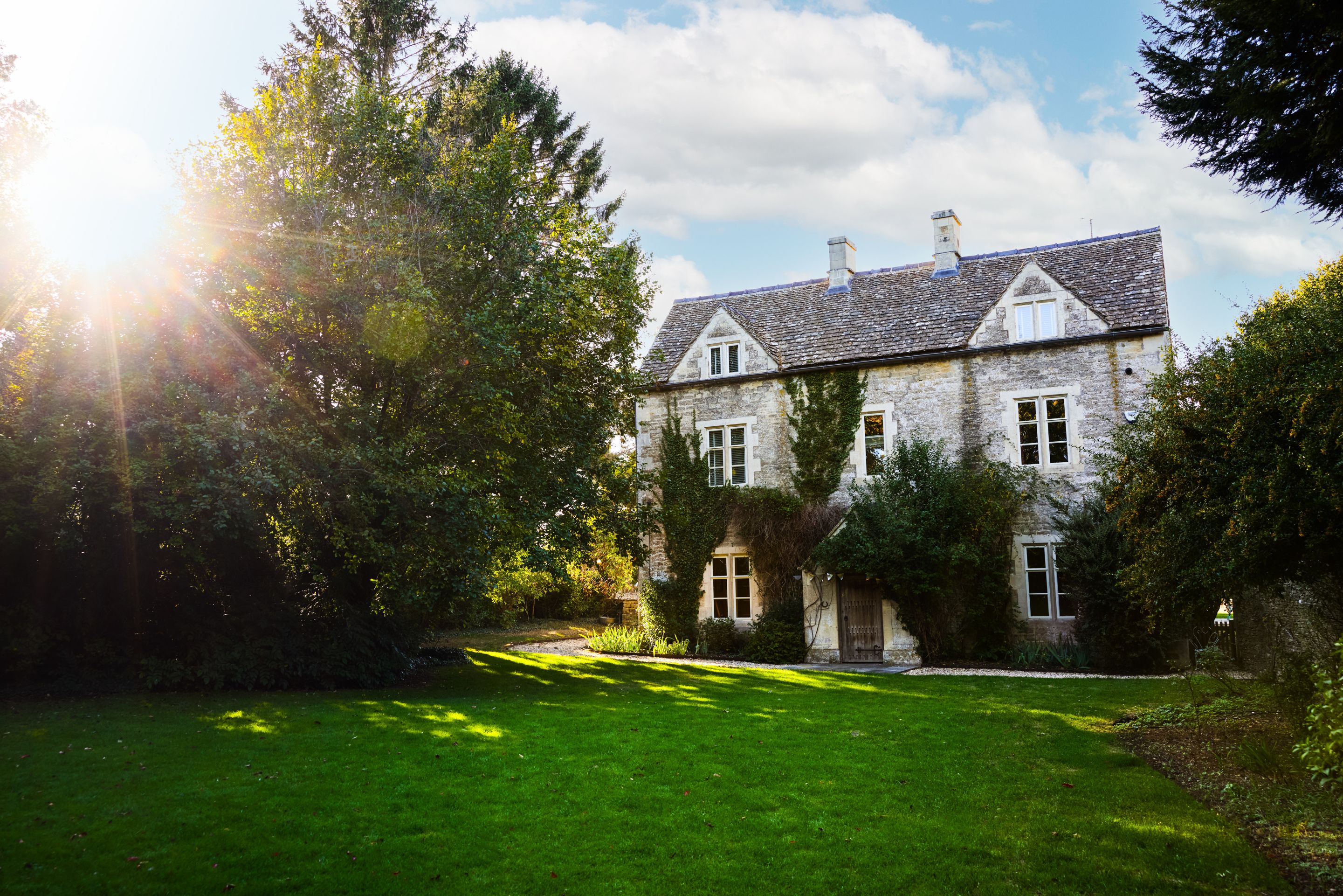 A large stone building with a sloped roof, surrounded by lush greenery and a well-maintained lawn.