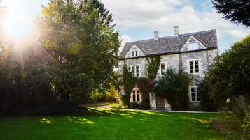 A large stone building with a sloped roof, surrounded by lush greenery and a well-maintained lawn.