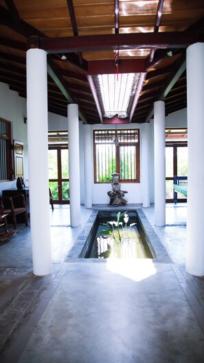 A serene indoor space with a central water feature, wooden beams, and a traditional stone statue. - 4 BR Hilltop Bungalow with 360° Mountain Views - Kandy Getaway (Kandy)