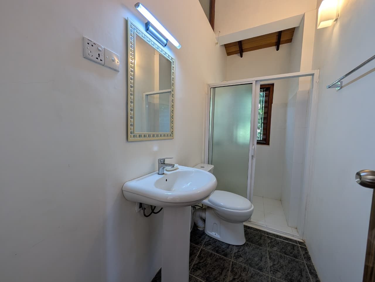 A bathroom with a white sink, a mirror, a toilet, and a shower area.