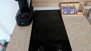 A kitchen with a black coffee maker, a built-in induction cooktop, and a wooden spice rack. - Chateau apartment (Aheloy)