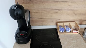 Een keuken met een zwart inductiefornuis, een koffiezetapparaat en een houten kast met vakken.