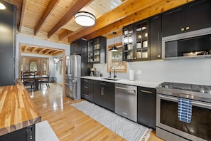 A modern kitchen with dark cabinetry, stainless steel appliances, and a wooden ceiling.