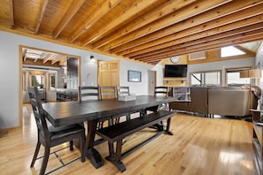 A spacious dining area with a long table and benches, a kitchen area with cabinets and a stove, and a living area with a sofa and a television.