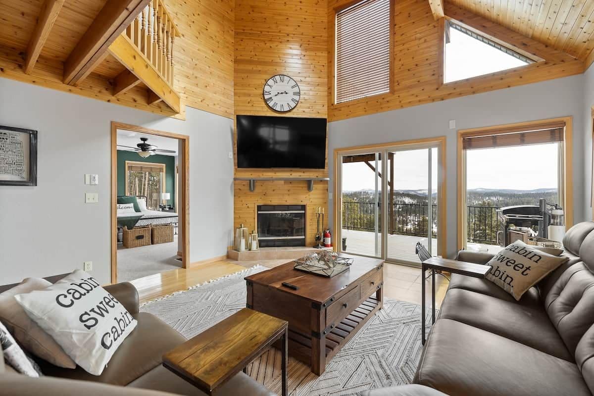L’intérieur d’une cabane avec un plafond en bois, une cheminée, un téléviseur et un canapé agrémenté de coussins.