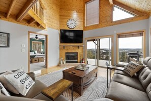 A cabin interior with a wooden ceiling, a fireplace, a television, and a sofa with pillows.