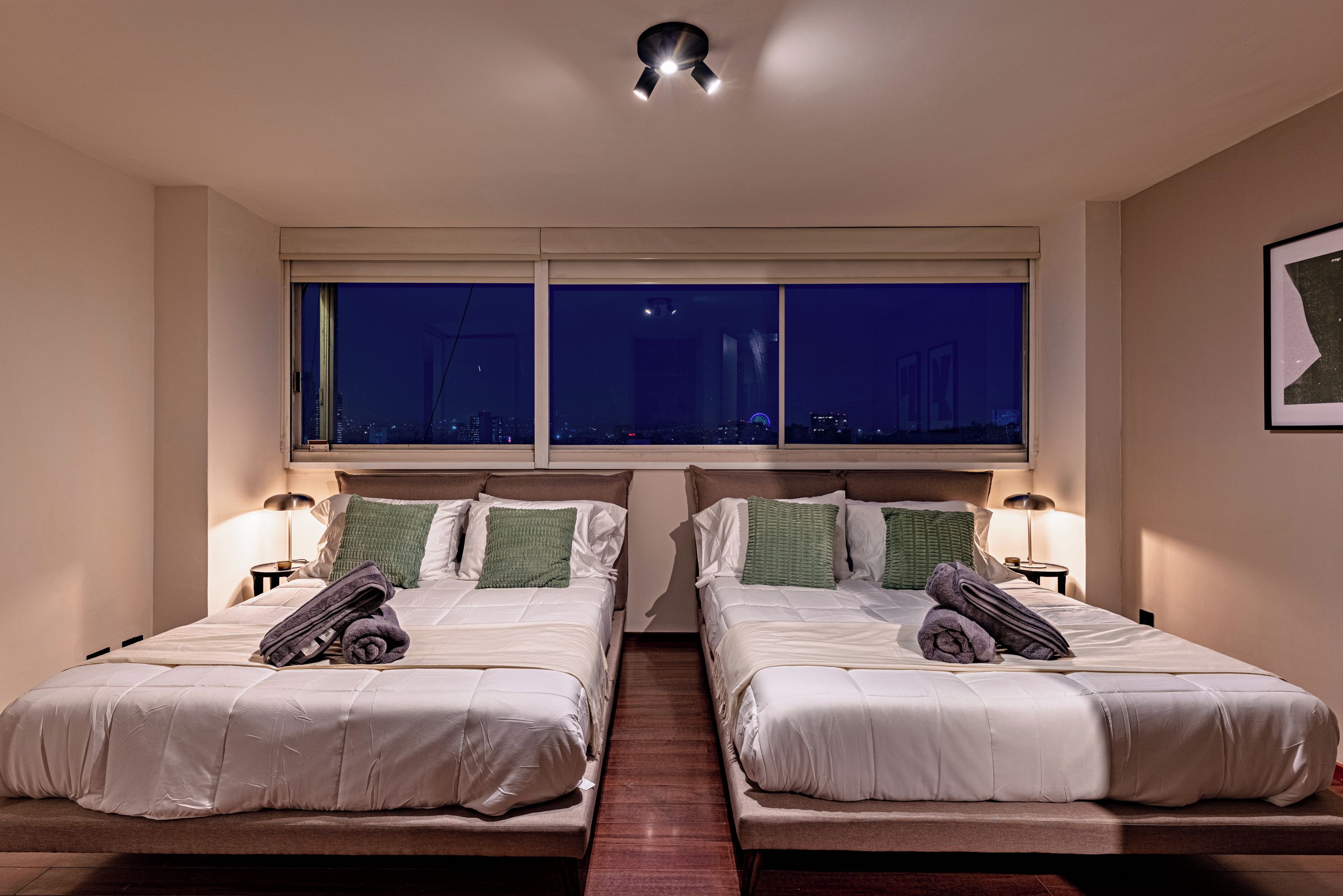 Une chambre d’hôtel avec deux lits, une grande fenêtre donnant sur la ville et un luminaire au plafond.