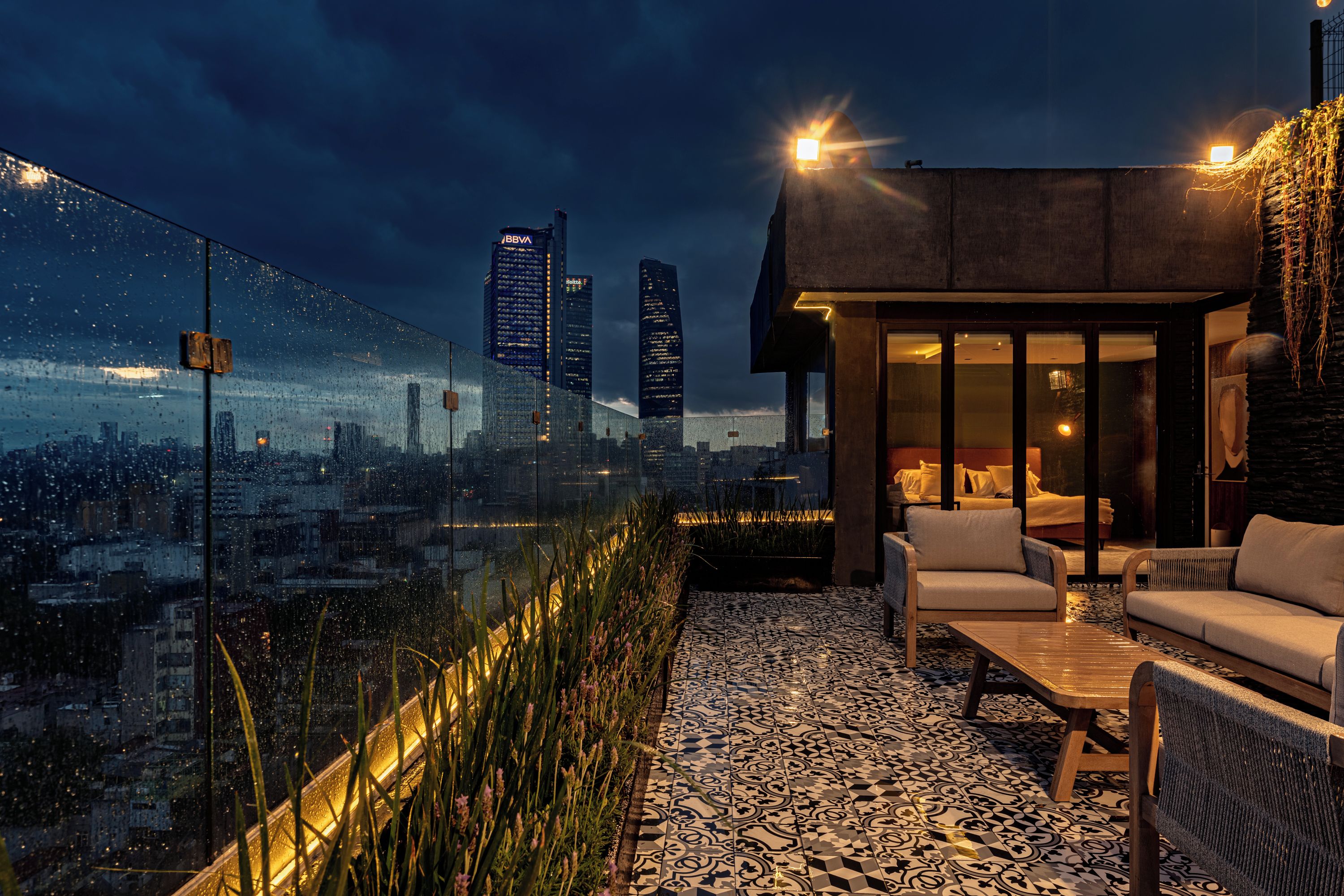 Una terraza en la azotea con vistas a la ciudad, mobiliario exterior y una estructura de edificio moderna.