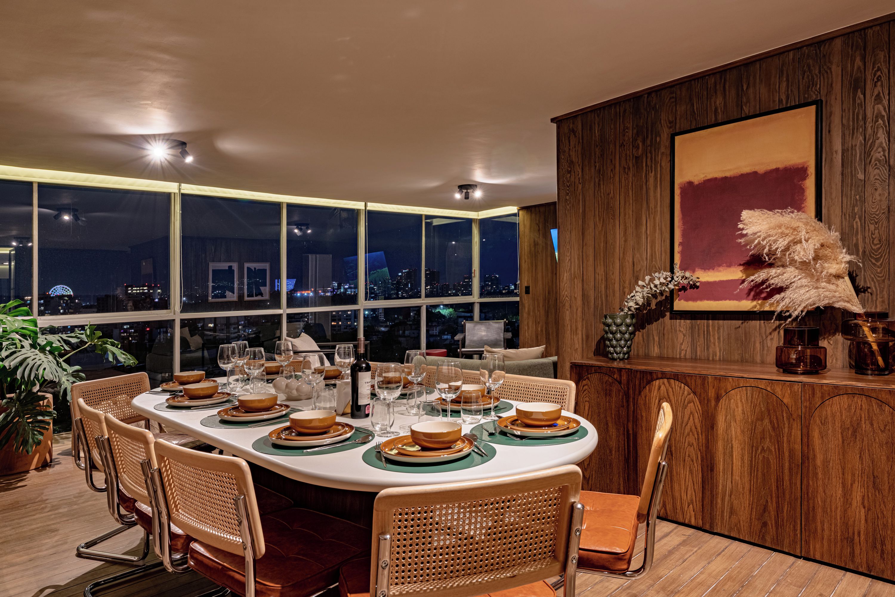Ein Essbereich mit Blick auf die Stadt, ein großer Tisch gedeckt für eine Mahlzeit und eine Wand mit Holzvertäfelung und einem Gemälde.