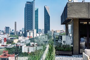 Ein Hochhaus mit moderner Glasfassade, einer Dachterrasse mit Sitzgelegenheiten und einer Stadtansicht im Hintergrund.