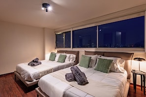 Ein Hotelzimmer mit zwei Betten, einem Nachttisch, einer Lampe und einem großen Fenster mit Blick auf die Stadt.