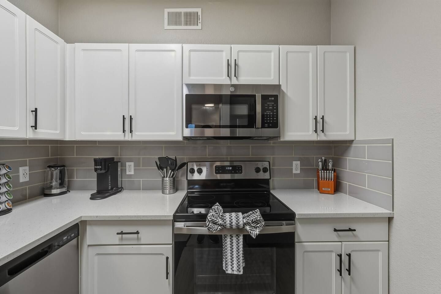 A kitchen with white cabinets, a microwave, a stove, and a coffee maker.