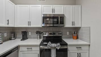 A kitchen with white cabinets, a microwave, a stove, and a coffee maker.