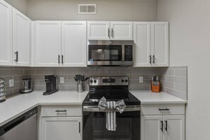 A kitchen with white cabinets, a microwave, a stove, and a coffee maker. - Cozy 2BR | 2BA • Pool • Gym • Free Parking A1 (Phoenix)
