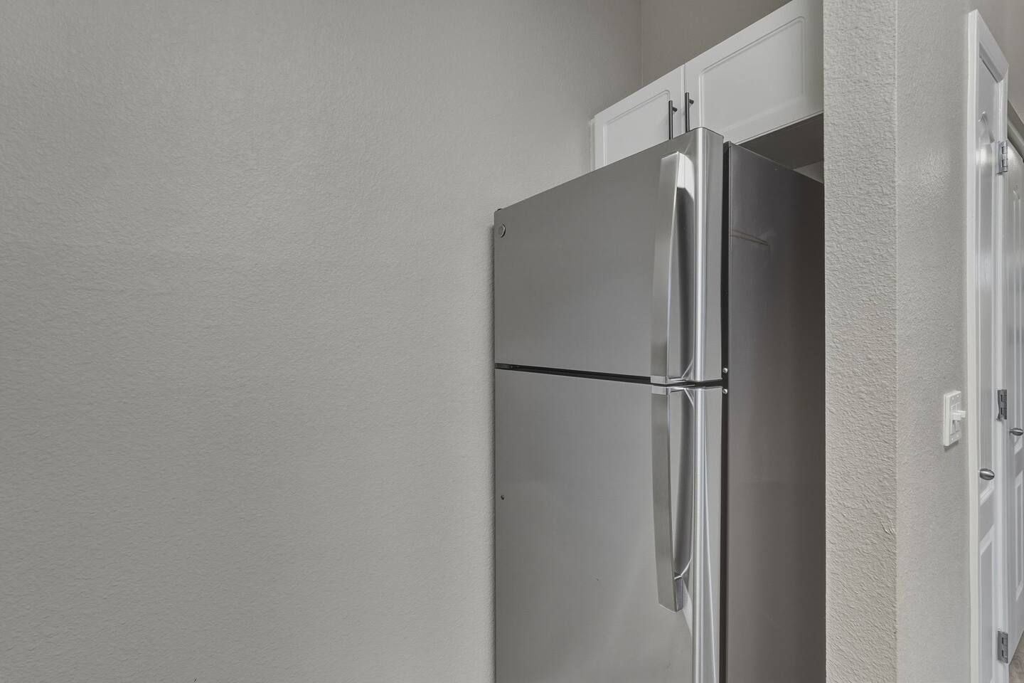 Ein Edelstahl-Kühlschrank mit einem darüberliegenden weißen Schrank, eingebaut in eine Küche mit weißen Wänden.