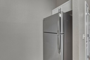 Ein Edelstahl-Kühlschrank mit einem darüberliegenden weißen Schrank, eingebaut in eine Küche mit weißen Wänden.