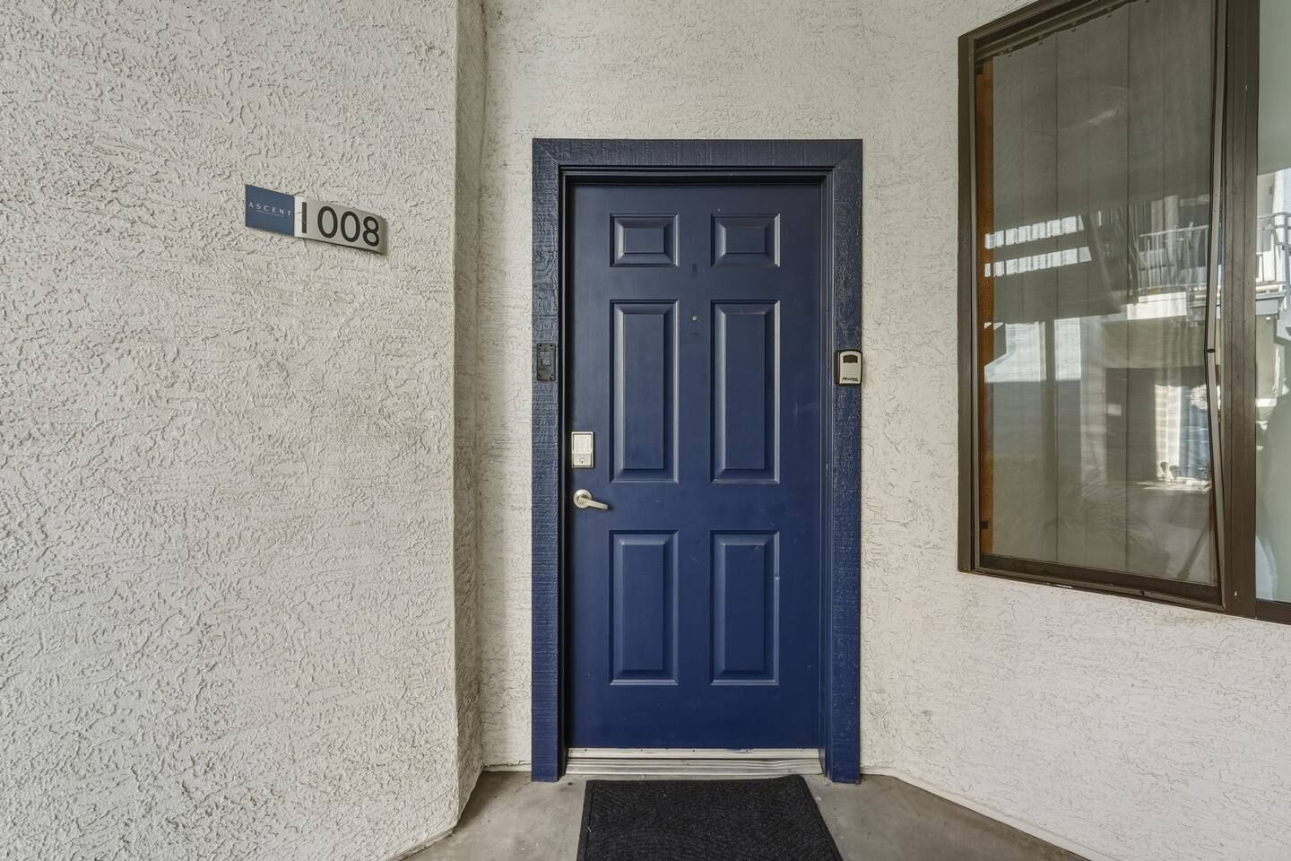 Uma porta azul com uma placa de identificação que diz '1008' e um tapete de entrada.