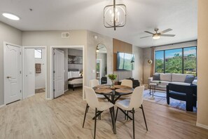 A modern living room with a dining area, a large window with a view, and a ceiling fan. - Cozy 2BR | 2BA • Pool • Gym • Free Parking A1 (Phoenix)