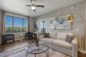 Ein modernes Wohnzimmer mit einer Couch, Sesseln, einem Couchtisch, einer Stehlampe und einem Deckenventilator.