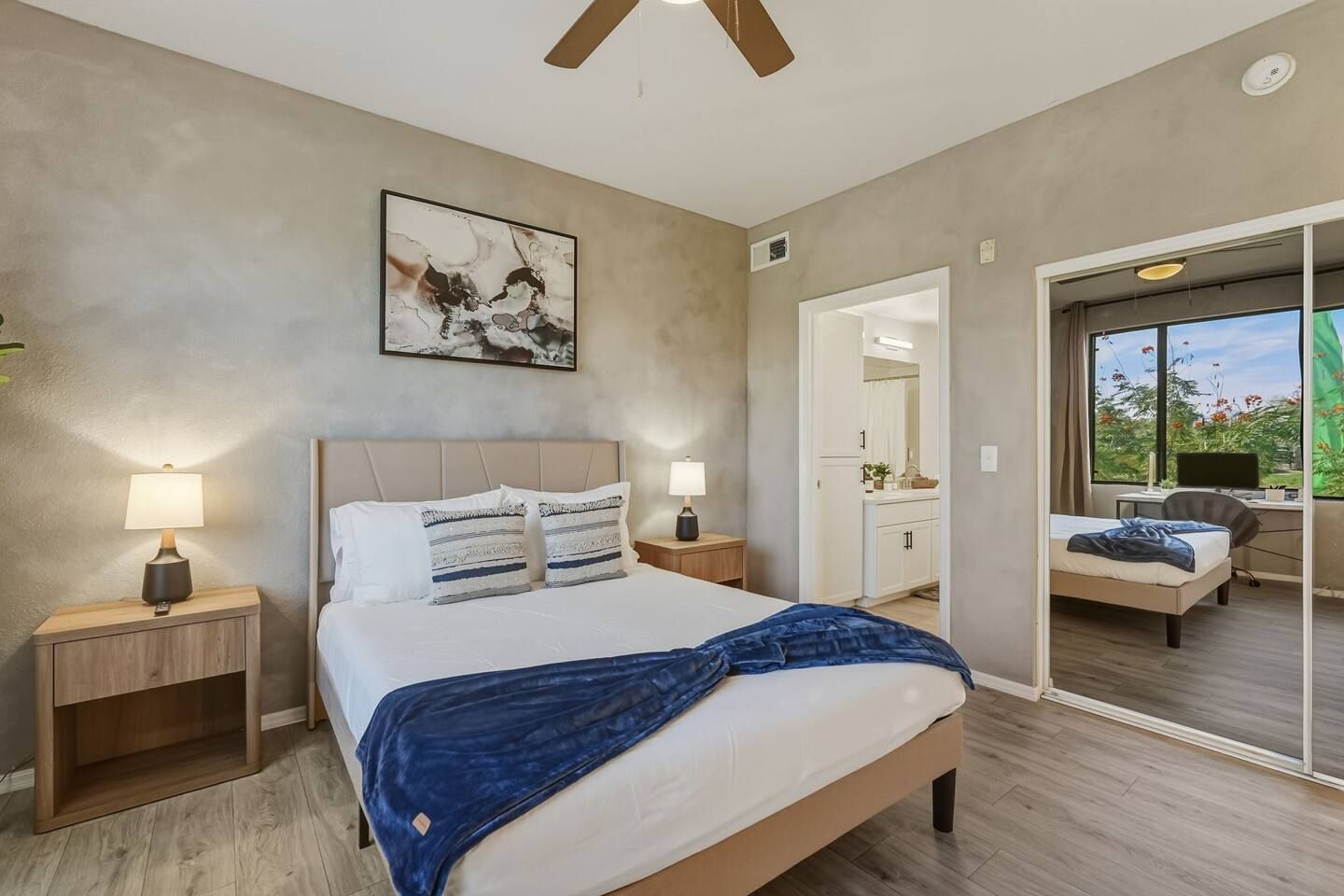 Ein Schlafzimmer mit einem Bett, Nachttischlampen, einem Deckenventilator, einem Gemälde und Blick auf einen Balkon.