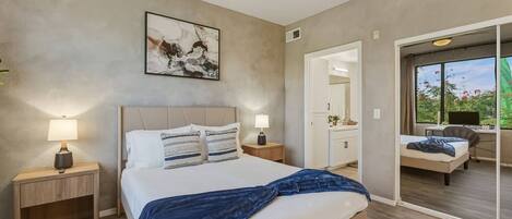 A bedroom with a bed, bedside lamps, a ceiling fan, a painting, and a view of an outdoor balcony.