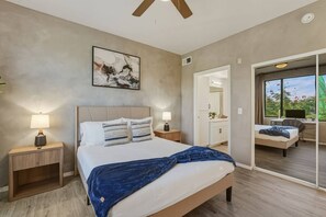 Ein Schlafzimmer mit einem Bett, Nachttischlampen, einem Deckenventilator, einem Gemälde und Blick auf einen Balkon.