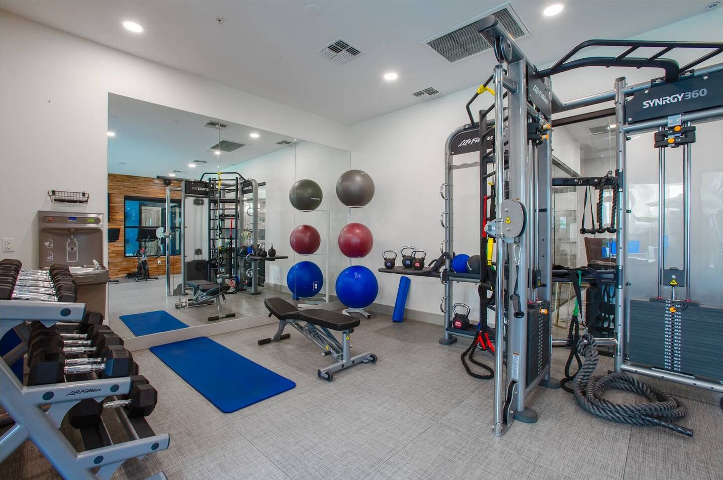 A gym with weightlifting equipment, exercise balls, and a squat rack.
