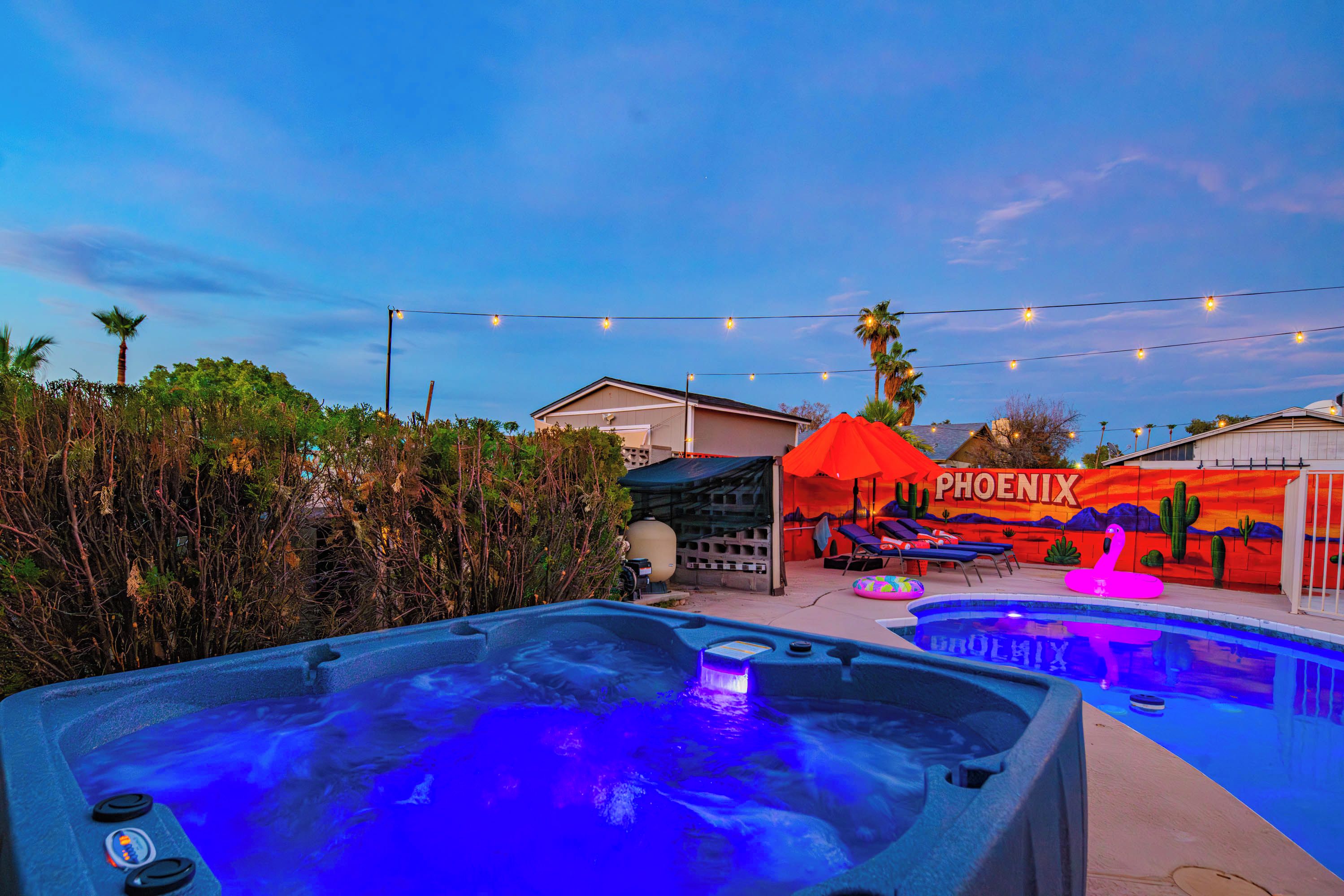 A pool area with hot tubs, a mural with the word 'PHOENIX,' and string lights.