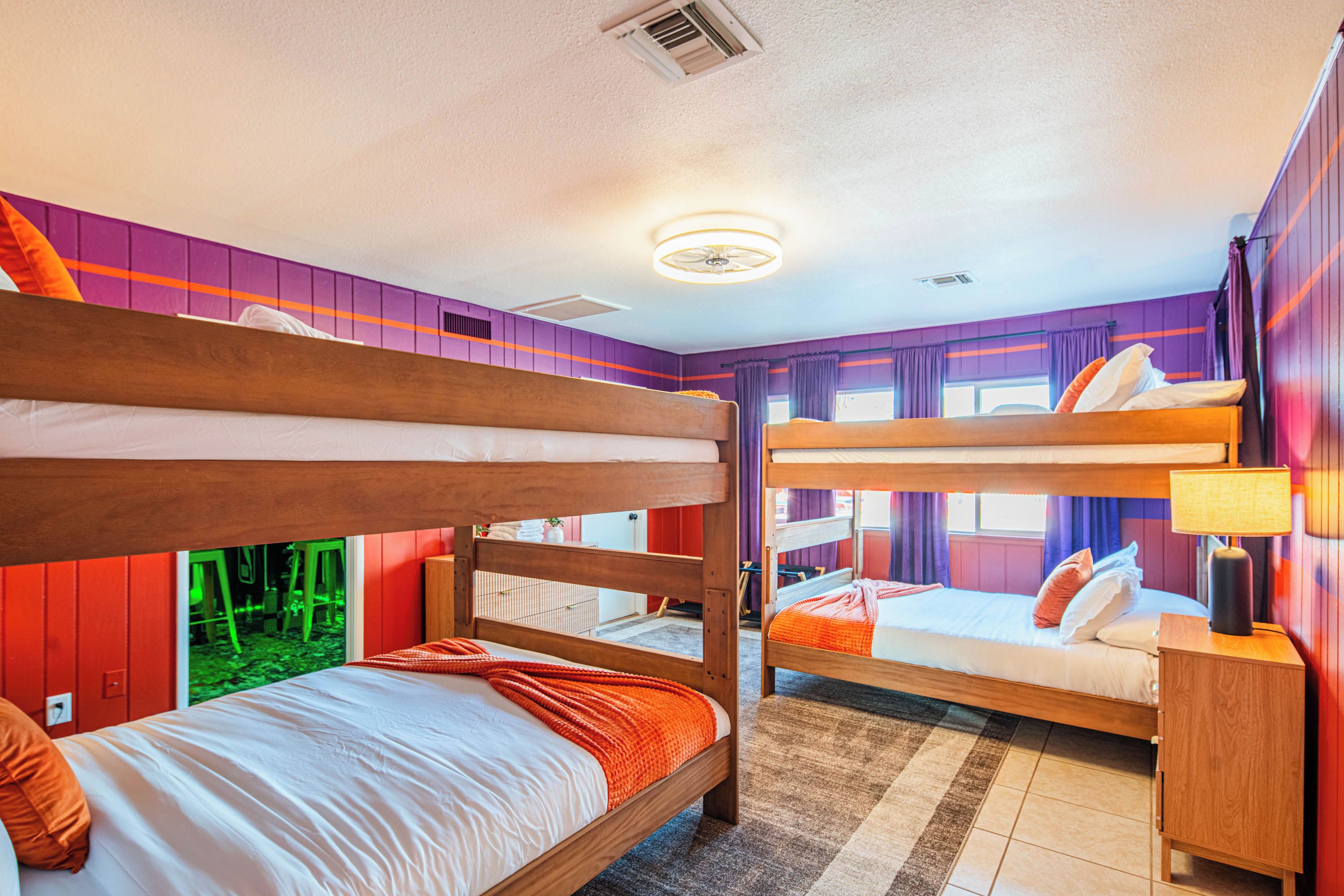 Quarto com beliche, cabeceira de madeira, mesa de cabeceira com luminária e janela com cortinas.