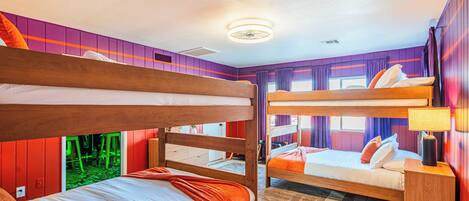 A bunk bed room with a wooden headboard, a bedside table with a lamp, and a window with curtains.